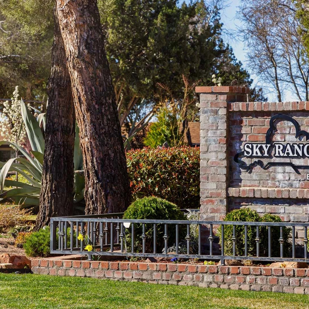 Brick sign reading 'Sky Ranch Lodge Botanical Garden' surrounded by trees and plants.