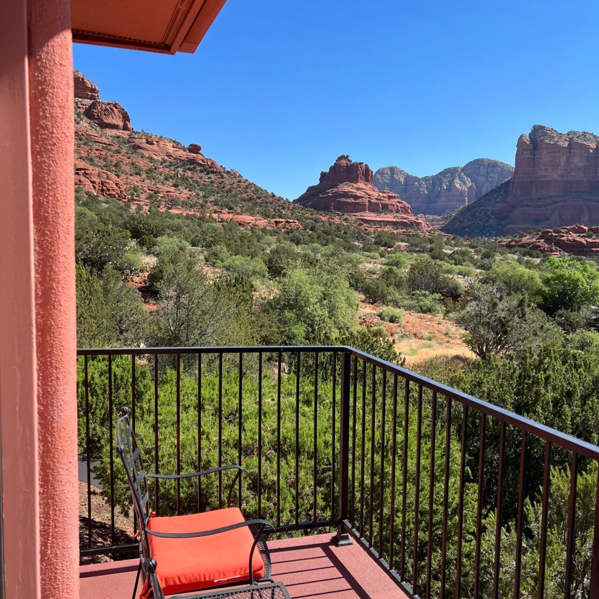Balcony with orange chairs overlooking red rock desert landscape under clear blue sky.