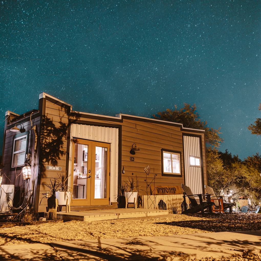 Tiny house at night with starry sky background and porch lights glowing.
