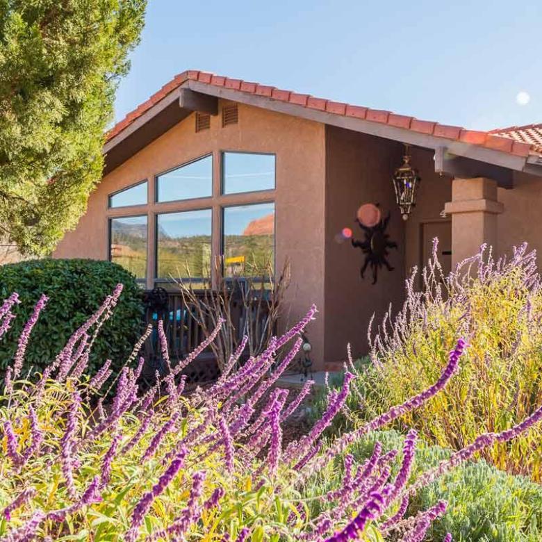 House with red-tiled roof, large windows, and purple flowers in the foreground.